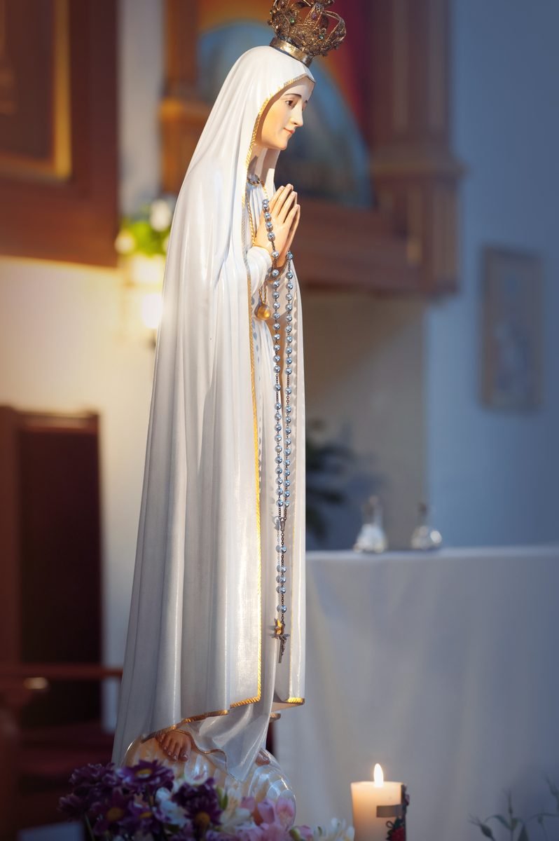 A statue of Our Lady with a rosary, before a lit candle