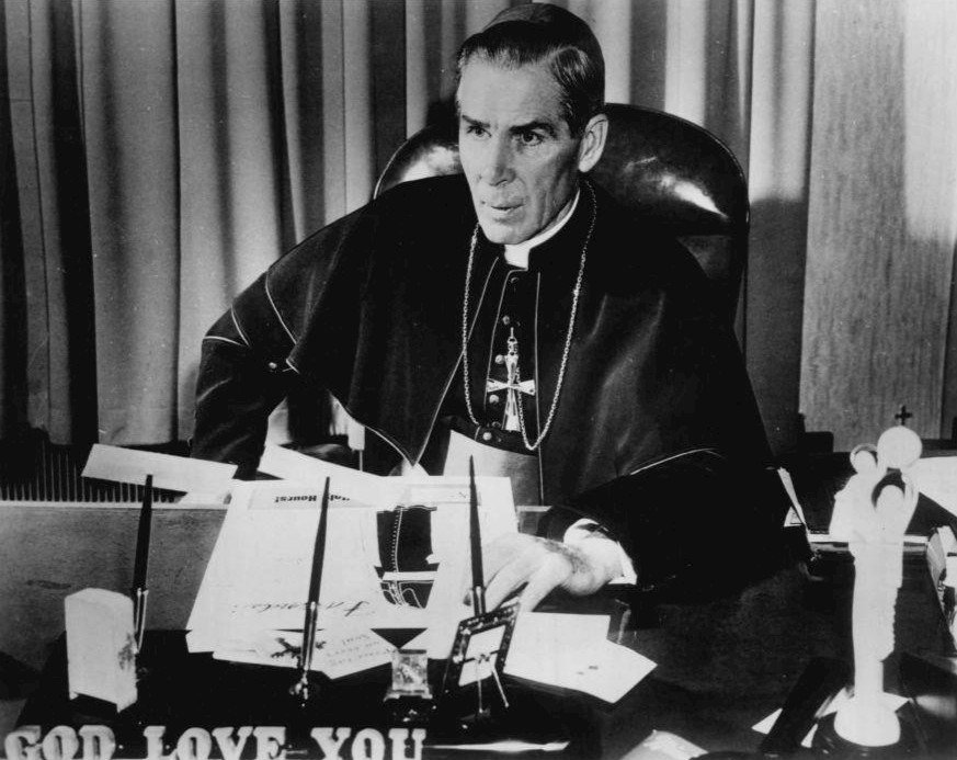 Archbishop Sheen at his desk beneath the words God Love You